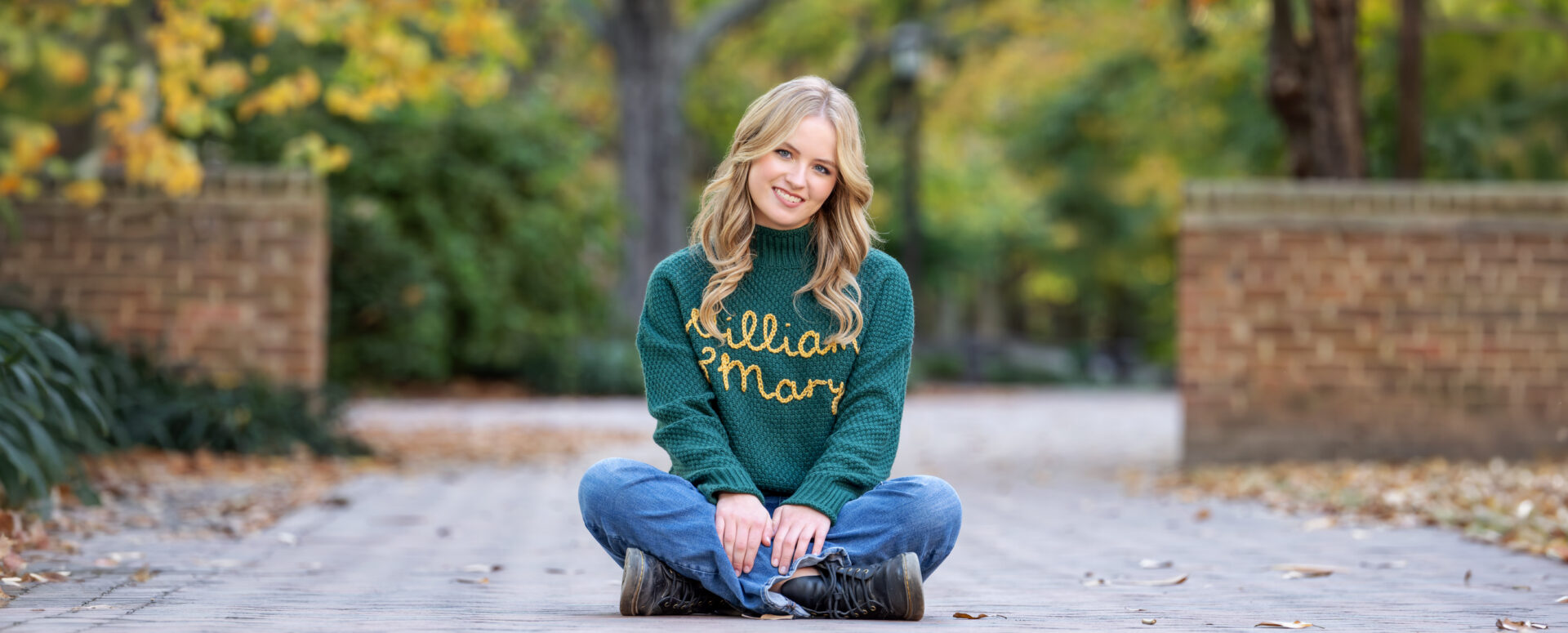 A photo of a high school senior girl sitting on William & Mary campus wearing a green William & Mary sweater, taken by Marika H Photography in Williamsburg, VA