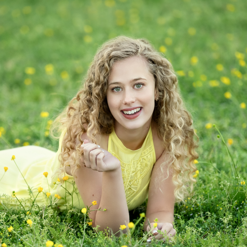 Picture of a high school senior girl laying in a field of buttercups in Williamsburg, VA, taken by Marika H Photography